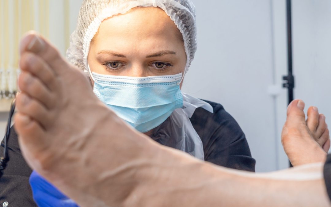 A masked doctor inspects a patient's foot and leg.